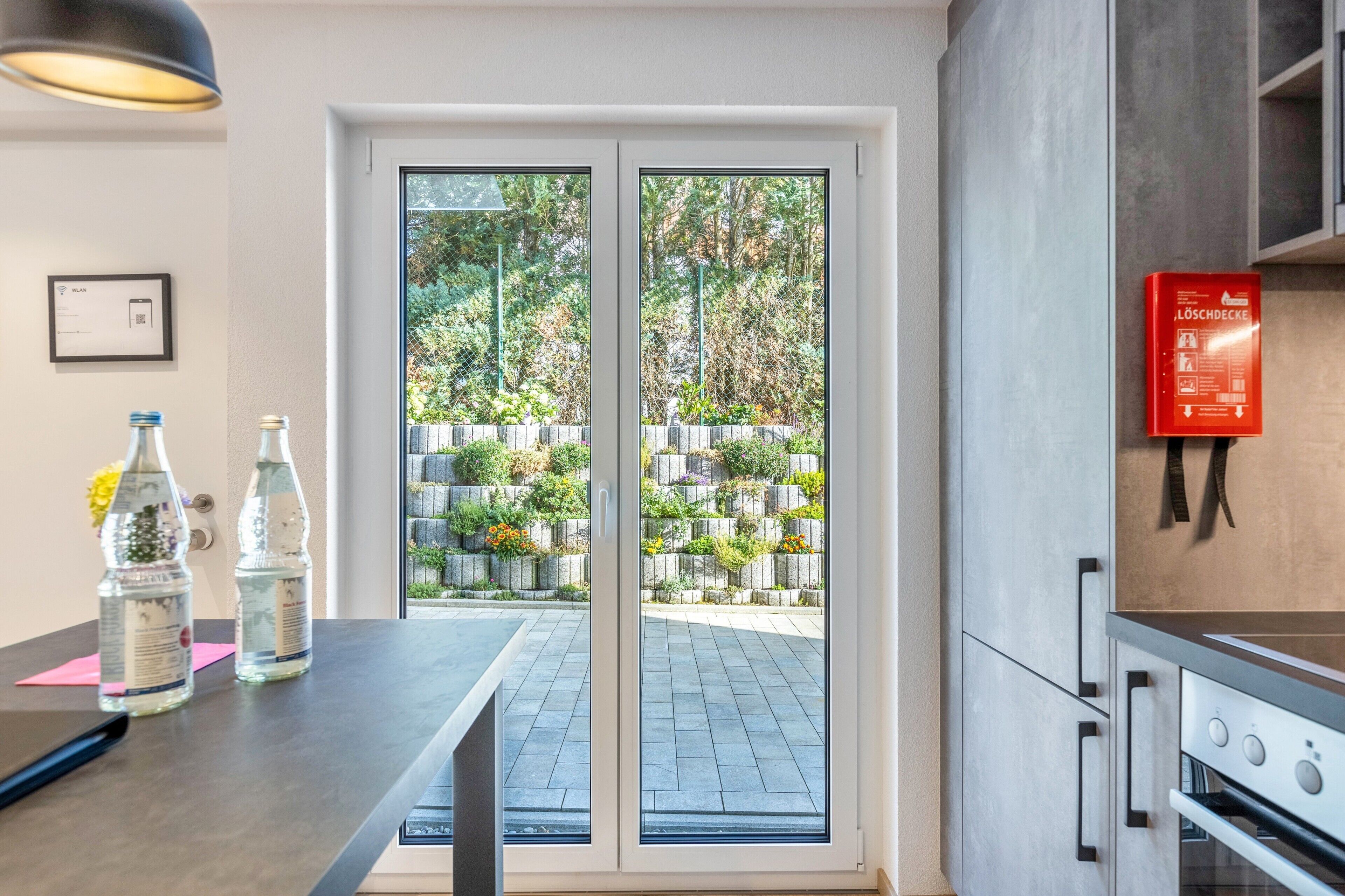 Eine moderne Küche mit Backofen, Wasserspender und Glastür zu einem Gartenbereich.