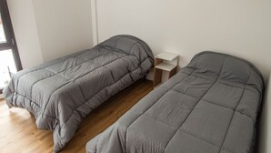 Ein Zimmer mit zwei Einzelbetten, einem kleinen Nachttisch und einem Fenster.