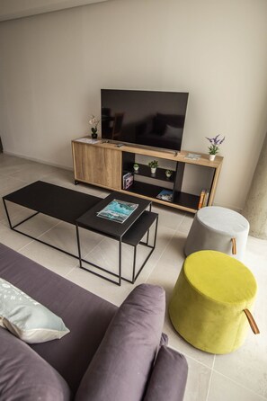 Moderni olohuone, jossa on sohva, sohvapöytä, TV-taso ja pieni pyöreä jalkarah.