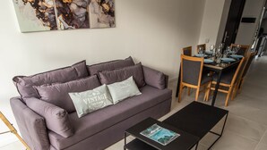 Ein modernes Wohnzimmer mit Sofa, Couchtisch und Essbereich mit Stühlen und Tisch für vier Personen.