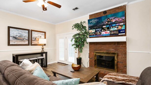 Una sala de estar con chimenea, televisor montado arriba, ventilador de techo y comedor con mesa y sillas.