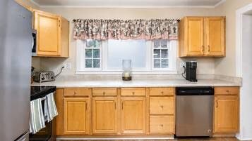 A kitchen with wooden cabinets, a stainless steel dishwasher, and a window with a patterned valance.