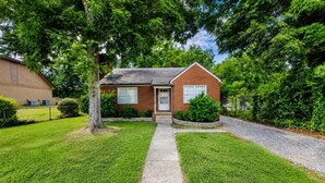 A single-story brick house with a front porch, a lawn, and a driveway leading to the entrance. - The Fig · Family Home + Fenced Yard Near Elon U (Burlington)