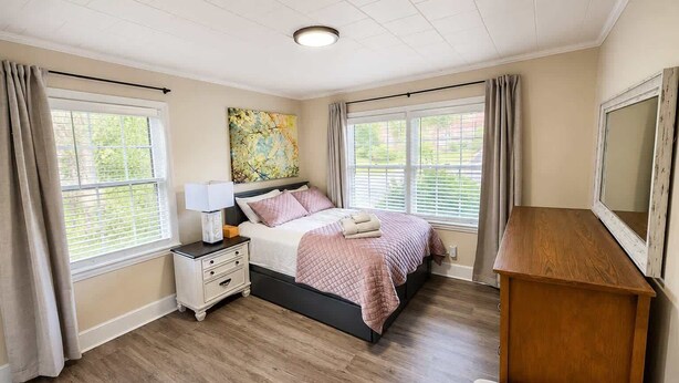 A bedroom with a bed, bedside table, lamp, and a wooden dresser. - The Fig · Family Home + Fenced Yard Near Elon U (Burlington)