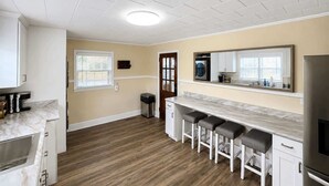 A kitchen with a marble countertop, wooden flooring, a built-in oven, a refrigerator, and a window with blinds. - The Fig · Family Home + Fenced Yard Near Elon U (Burlington)