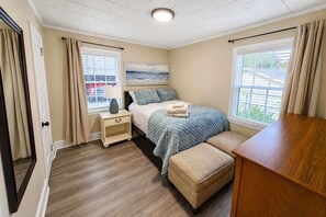 Un dormitorio con cama, mesita de noche, lámpara y vistas al exterior a través de la ventana.