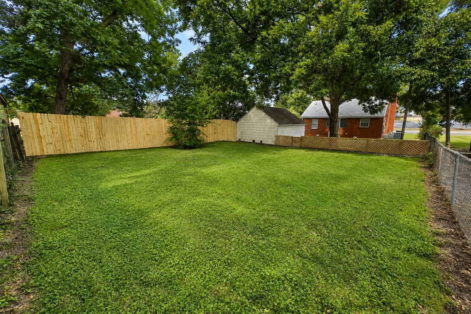 A well-maintained backyard with a wooden fence, a small shed, and a house in the background.