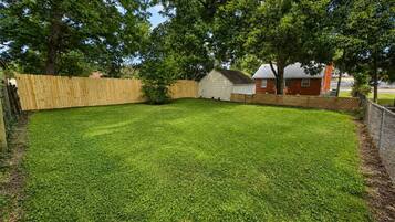A well-maintained backyard with a wooden fence, a small shed, and a house in the background.