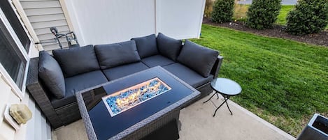 Un patio al aire libre con un sofá de color oscuro, una mesa de centro de vidrio y una pequeña mesa redonda.