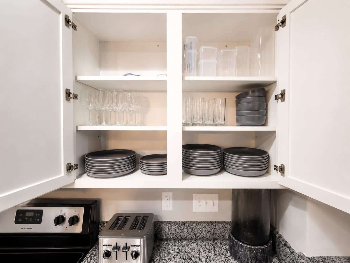 A kitchen with a built-in toaster, a stove, and cabinets containing plates and glasses.