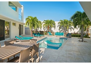 A modern outdoor pool area with lounge chairs and a dining table, surrounded by palm trees and a clear blue sky. - Pool Villa 1 Steps From Jimmy Hill Beach Beautiful Water Views WEST TOWER ONLY (Moss Town)