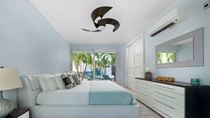 A modern bedroom with a bed, a dresser, a mirror, and an air conditioning unit. - Luxury Pool Villa 50 Steps From Stunning Beach Beautiful Views WEST TOWER ONLY (Moss Town)