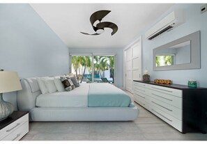 A modern bedroom with a bed, a dresser, a mirror, and an air conditioning unit. - Luxury Pool Villa 50 Steps From Stunning Beach Beautiful Views WEST TOWER ONLY (Moss Town)