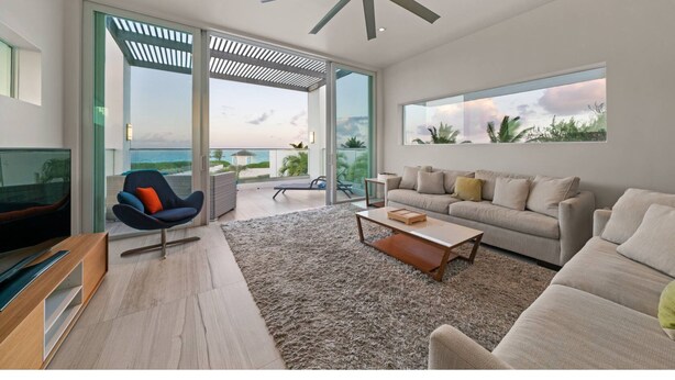 A modern living room with a large window, a ceiling fan, and a sofa. - Luxury Pool Villa 50 Steps From Stunning Beach Beautiful Views WEST TOWER ONLY (Moss Town)