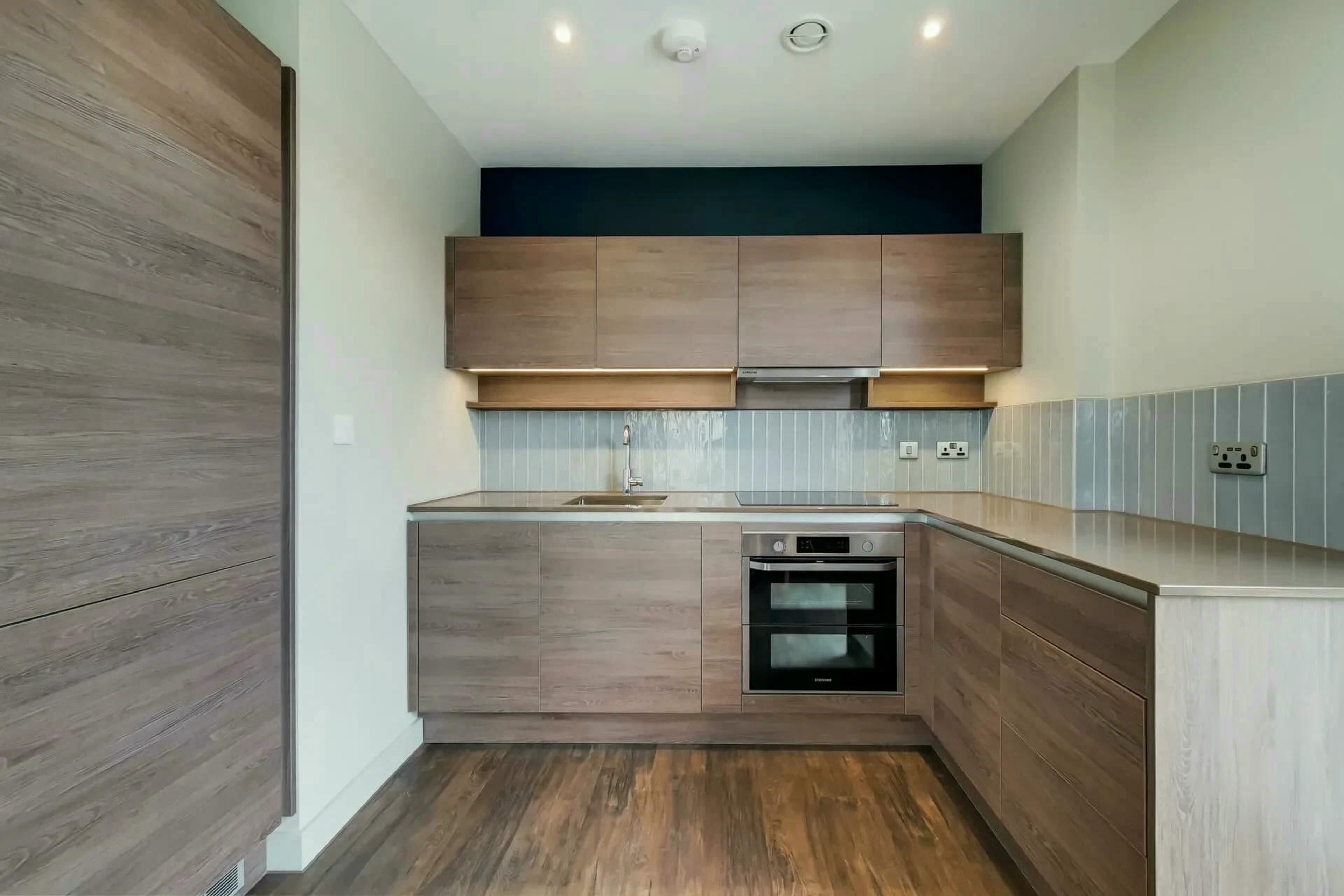 Eine kleine Küche mit Holzschränken, einem eingebauten Ofen und einer Edelstahl-Spüle.