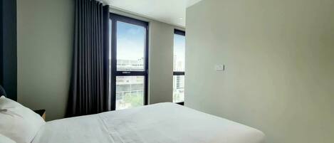 Una habitación de hotel con una cama grande, una ventana con cortinas y vistas a la ciudad.