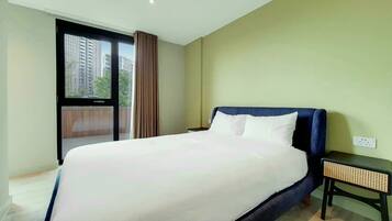A hotel room with a large bed, a nightstand, a window with a view of buildings, and a ceiling light.