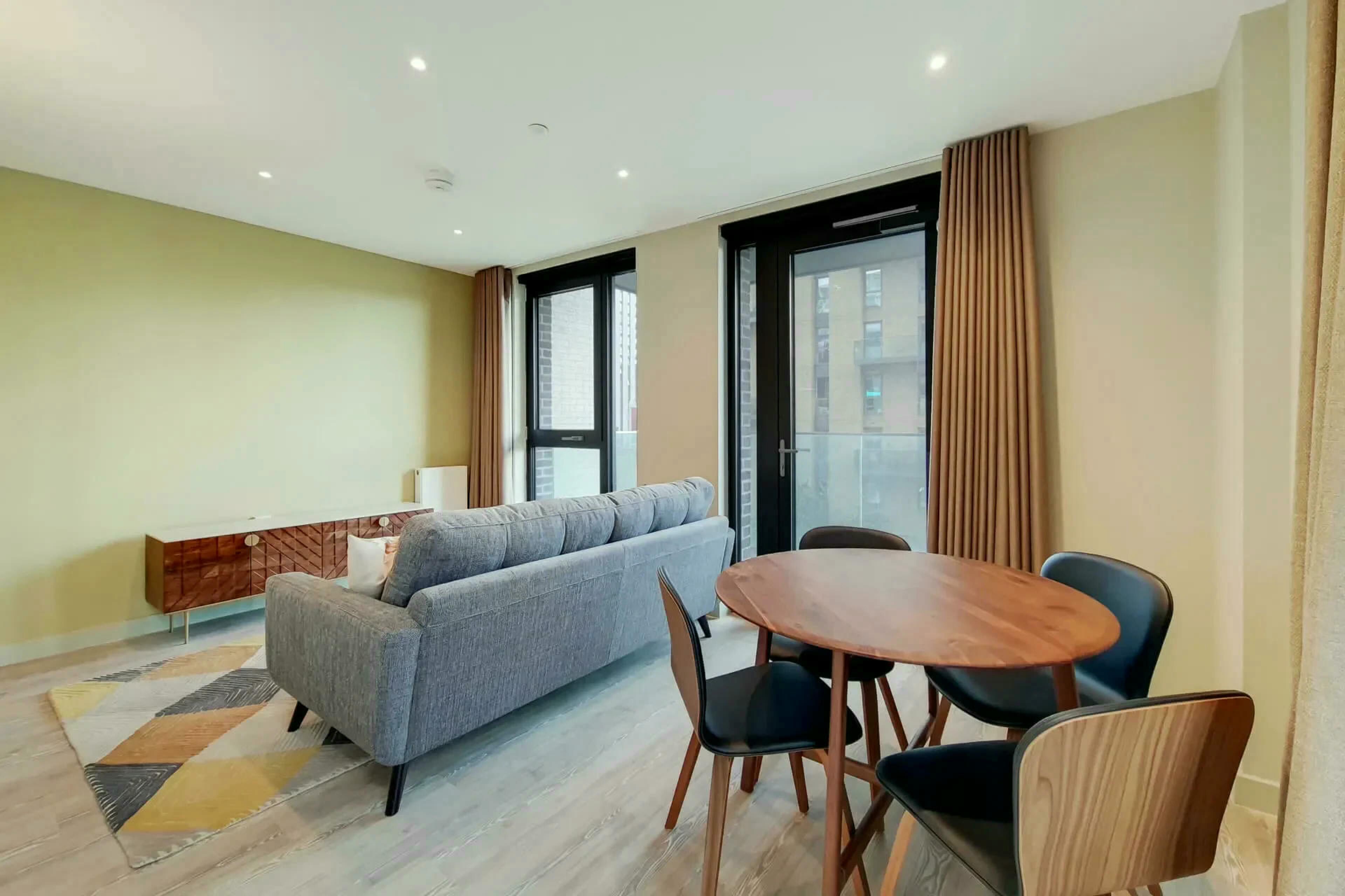 Een moderne woonkamer met een bank, een eettafel met stoelen, en een groot raam met gordijnen.