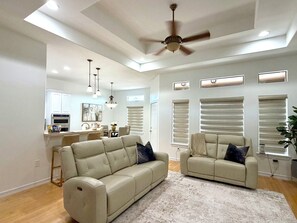 A spacious living room with a ceiling fan, two sofas, a dining area, and a kitchen in the background. - The Pinehurst Retreat - 3BR with Golf Course Views (Harlingen)