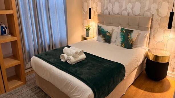 Ein Hotelzimmer mit Bett, Nachttisch, Lampe, Regal und Vorhang.