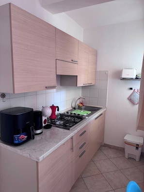 A kitchen with light wood cabinets, a gas stove, a coffee maker, and a toaster. - Fully furnished studio apartment across from Angulo Beach (Santa Maria)