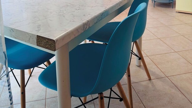 Ein Essbereich mit einem Marmortisch, blauen Stühlen, einem farbenfrohen abstrakten Gemälde und einer Holztür.
