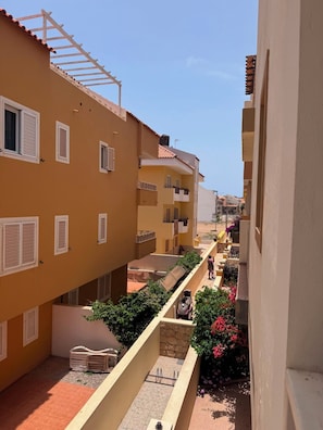 A narrow alleyway between buildings with balconies, a clear sky, and a person walking. - Fully furnished studio apartment across from Angulo Beach (Santa Maria)