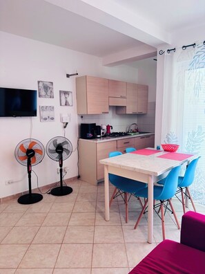 A compact kitchen with a dining area, two fans, and artwork on the walls. - Fully furnished studio apartment across from Angulo Beach (Santa Maria)