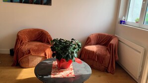 Et værelse med et rundt bord, to lænestole, en potteplante og et maleri på væggen.