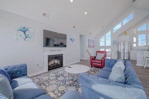 Ein geräumiges Wohnzimmer mit Kamin, einem roten Sessel, einem blauen Sofa und einem durchgehenden offenen Durchgang zum Küchenbereich.