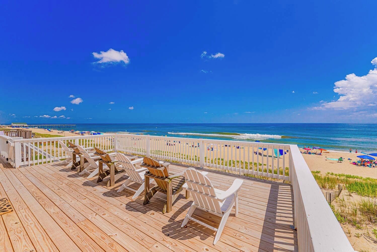 A wooden deck with chairs overlooking a beach with umbrellas and people.