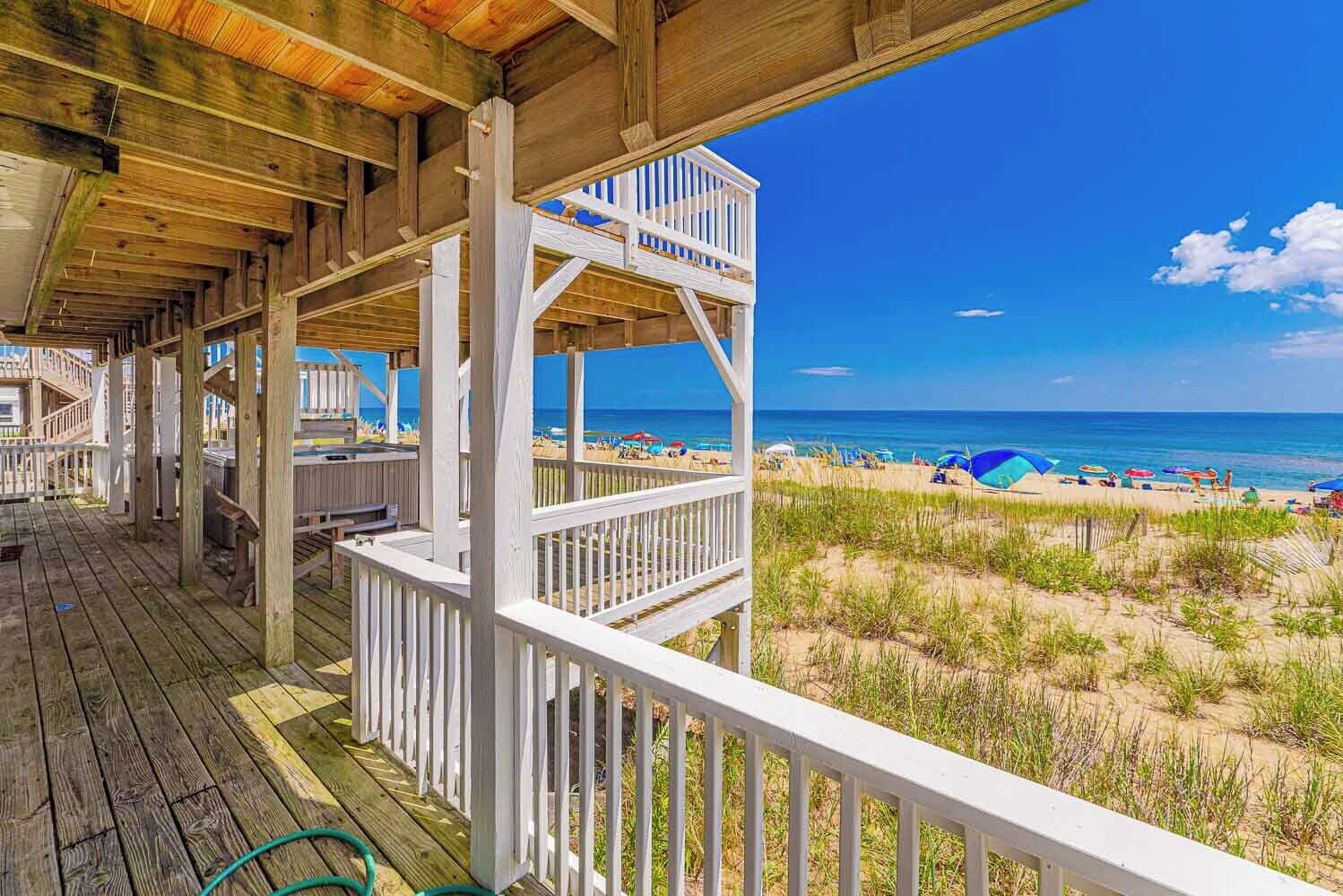 A wooden deck with a white railing overlooking a beach with umbrellas and people.