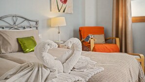 Un lit bien fait, avec des serviettes blanches disposées en forme de cygne, un oreiller vert, une lampe et un tableau représentant une tulipe accroché au mur.