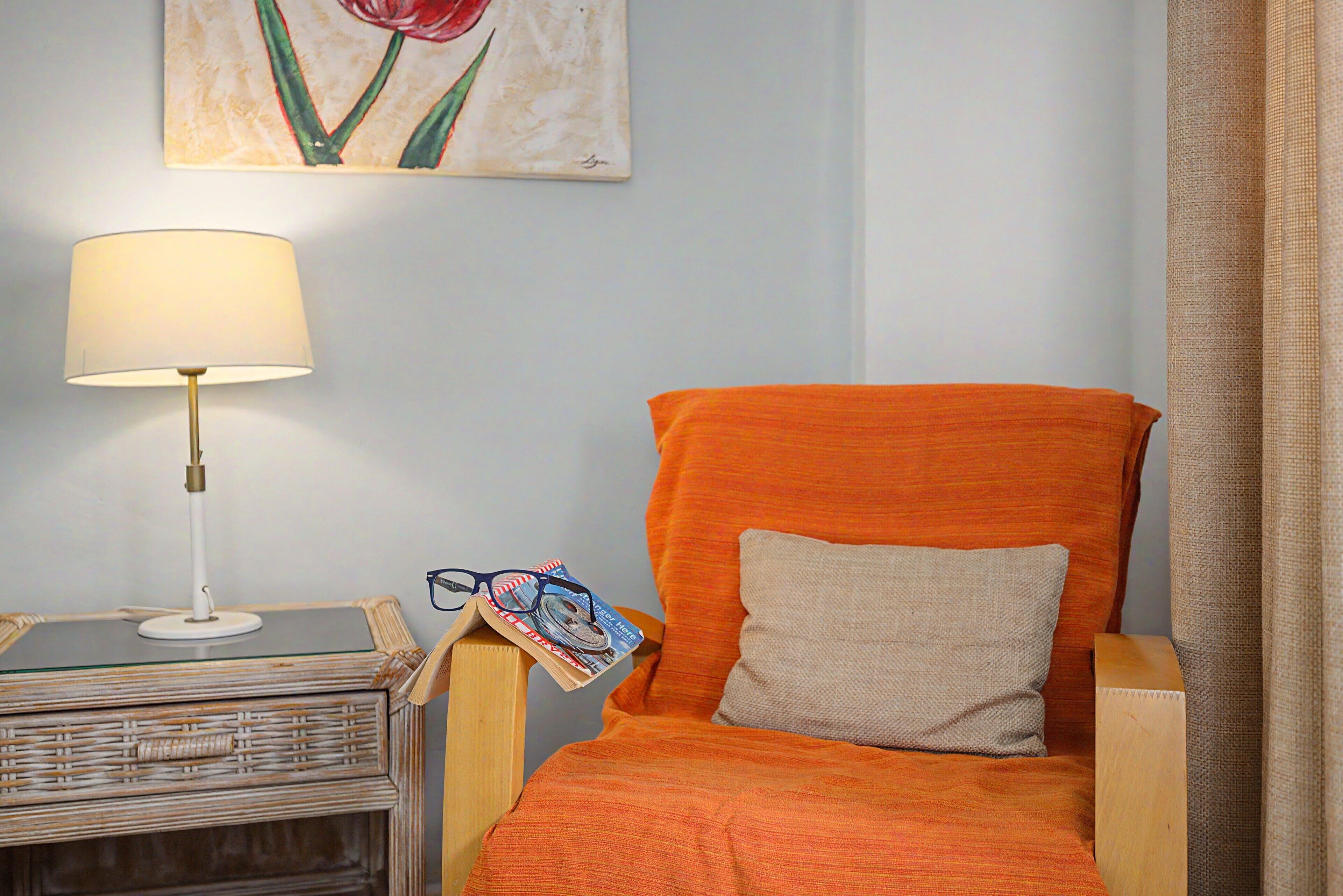 Ein Zimmer mit einem Holzstuhl, einer Lampe, einem kleinen Tisch und einem Bild an der Wand.