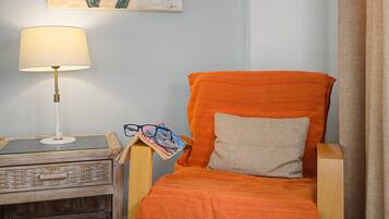 Ein Zimmer mit einem Holzstuhl, einer Lampe, einem kleinen Tisch und einem Bild an der Wand.