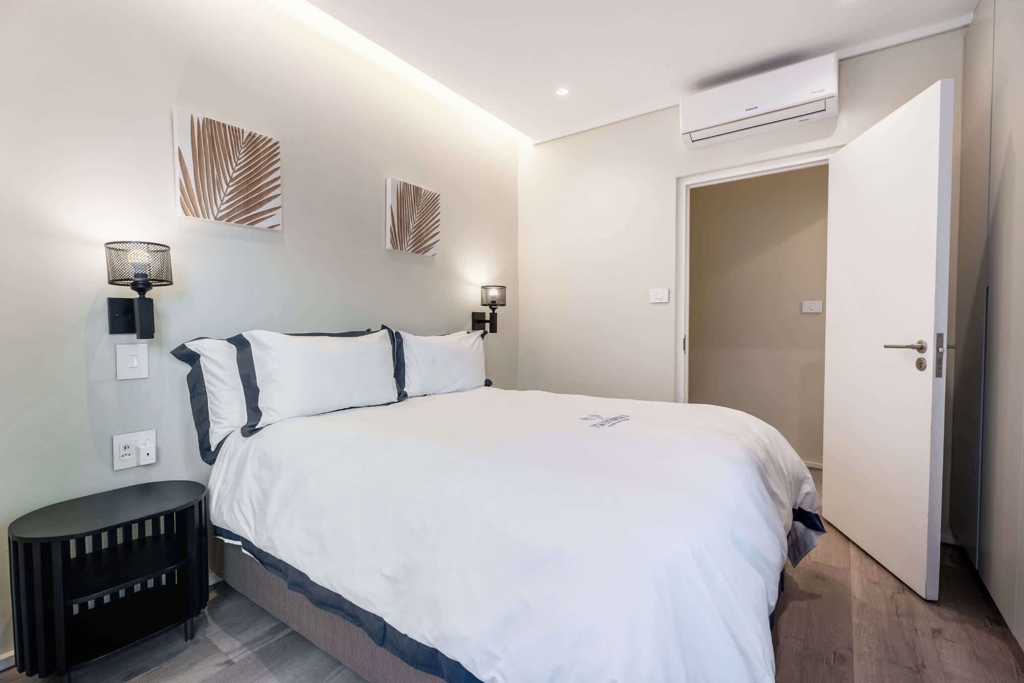 Ein Schlafzimmer mit einem Bett, Nachttischlampen, einer Wandklimaanlage und einer Tür zu einem anderen Raum.