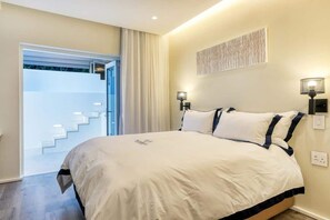 Ein Schlafzimmer mit einem großen Bett, einer Treppe zu einem Außenbereich und einer wandmontierten Lampe.