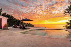 A swimming pool with lounge chairs and an umbrella, a pink building, and a sunset view. - Jacuzzi, Large Villa, 2 Pools, Camps Bay -Two Views (Cape Town)