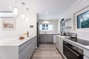 A modern kitchen with a central island, built-in appliances, and a window providing natural light. - Jacuzzi, Large Villa, 2 Pools, Camps Bay -Two Views (Cape Town)