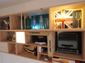 A wooden shelf with various items including bottles, glasses, a typewriter, and a ruler. - DOMUS ARTIS (Verona)
