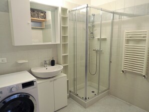 A bathroom with a glass-enclosed shower, a sink with a soap dispenser, a mirror, and a built-in washing machine. - DOMUS ARTIS (Verona)