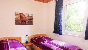 Ein Schlafzimmer mit zwei Betten, einem Nachttisch, einem Fenster mit Vorhängen und einem Bild von einem Pferd an der Wand.