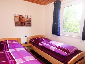 Ein Schlafzimmer mit zwei Betten, einem Nachttisch, einem Fenster mit Vorhängen und einem Bild von einem Pferd an der Wand.