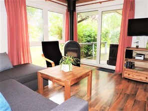 A cozy living room with a sofa, a wooden coffee table, a fireplace, and a television. - Moderner Doppelbungalow mit Terrasse und Grill im Ferienpark Mirow (Mirow)