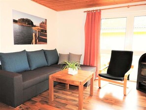 A living room with a sofa, a wooden coffee table, a chair, and a painting on the wall. - Moderner Doppelbungalow mit Terrasse und Grill im Ferienpark Mirow (Mirow)