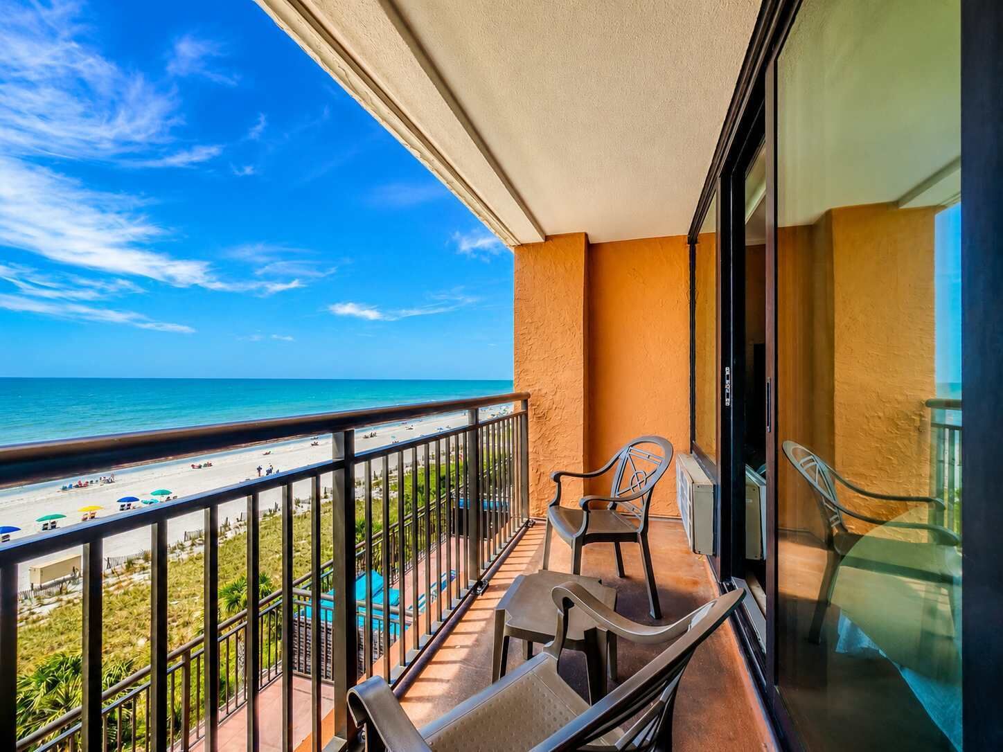 A balcony with a view of the beach and ocean, a chair, and a table.