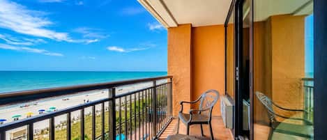 A balcony with a view of the beach and ocean, a chair, and a table.