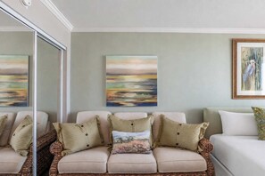 A living room with a beige sofa, two framed paintings, and a wicker coffee table. - Caravelle 624 Oceanfront Studio (Myrtle Beach)