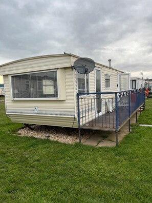 A mobile home with a satellite dish, a covered porch, and a fenced area. - Cabin Sleeps 6 With Pets Welcome (Skegness)