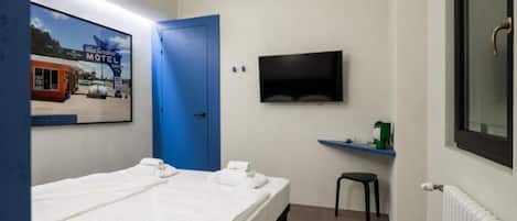 Een hotelkamer met twee bedden, een televisie, een blauwe deur en een lijst met een afbeelding aan de muur.